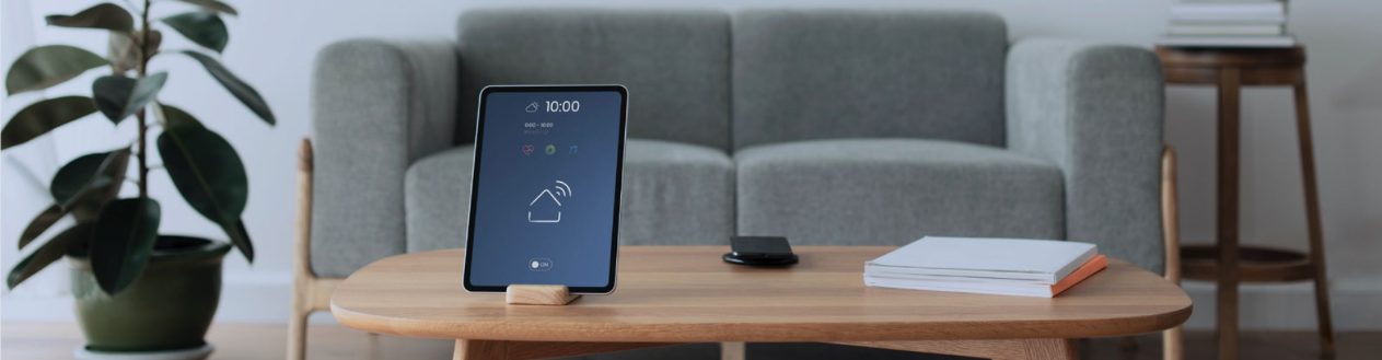 Jland website banner of a tablet with a smart-home icon on a wooden coffee table in a calm living room
