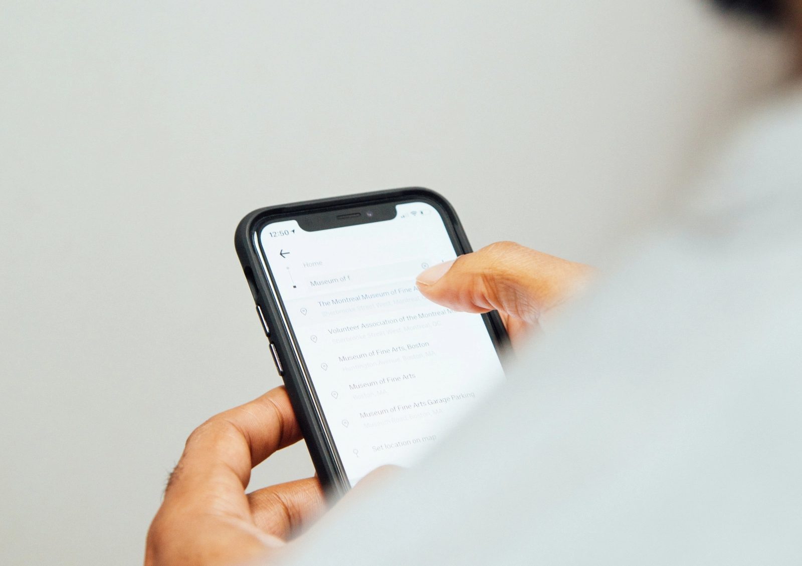 Hand holding a smartphone with a location search app open, representing mobile app development Malaysia by Spacebar