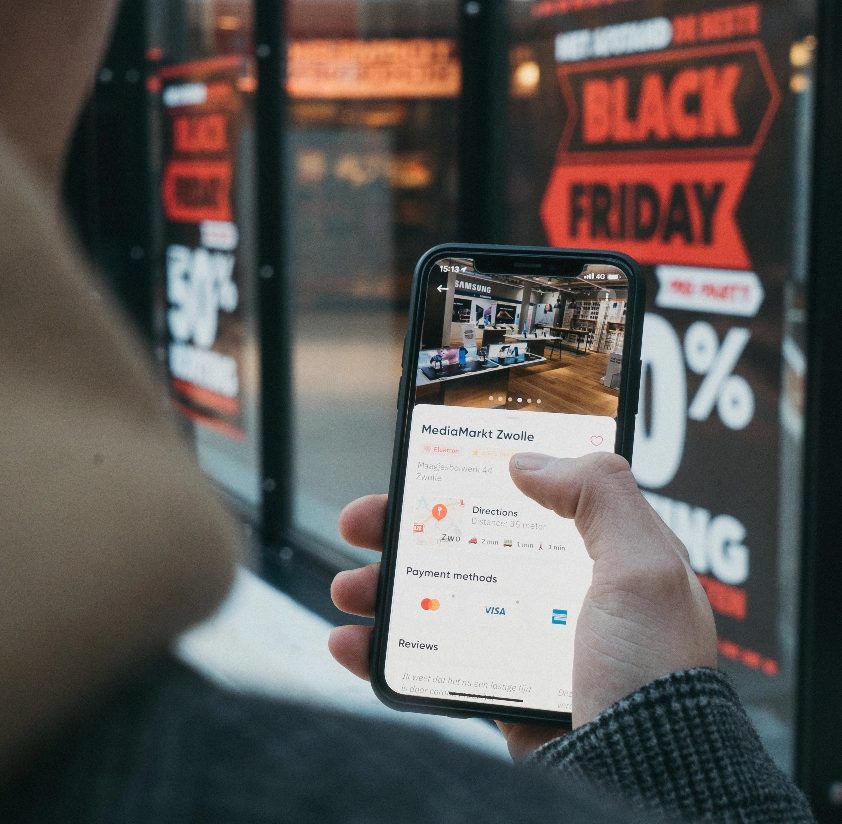 Shopper holding a smartphone with a store app open outside a shop window, illustrating ecommerce website design Malaysia